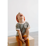 Laughing child in gray peace embroidered ringer tee and orange pants, ready to play