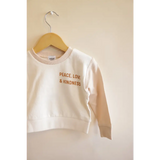 White Peace Love Kindness Pullover in Organic Cotton for Kids hanging on a hanger