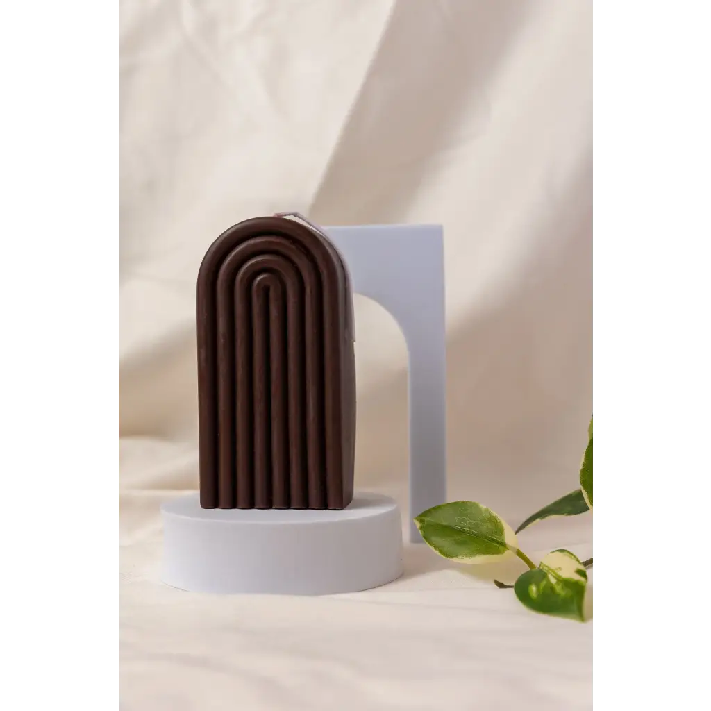 Brown arch-shaped sculpture with ridges next to a Petite Rainbow Candle for a colorful vibe