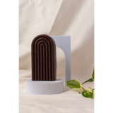 Brown arch-shaped sculpture with ridges next to a Petite Rainbow Candle for a colorful vibe
