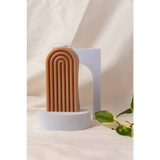 Terra cotta arch sculpture with grooves next to a Petite Rainbow Candle for colorful vibes