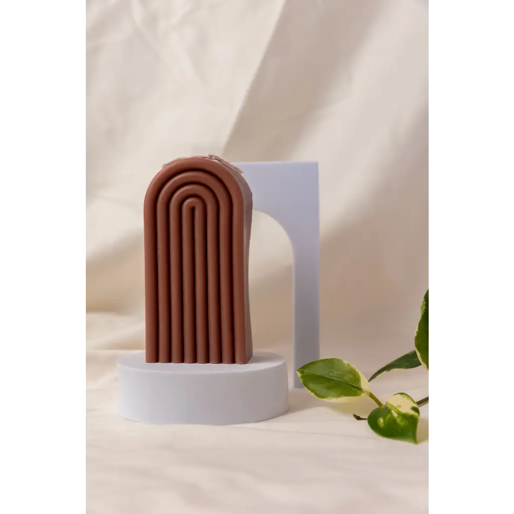 Brown terracotta arch sculpture on white pedestal with Petite Rainbow Candle for colorful vibes