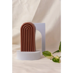 Brown terracotta arch sculpture on white pedestal with Petite Rainbow Candle for colorful vibes