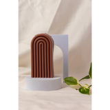 Brown terracotta arch sculpture on white pedestal with Petite Rainbow Candle for colorful vibes