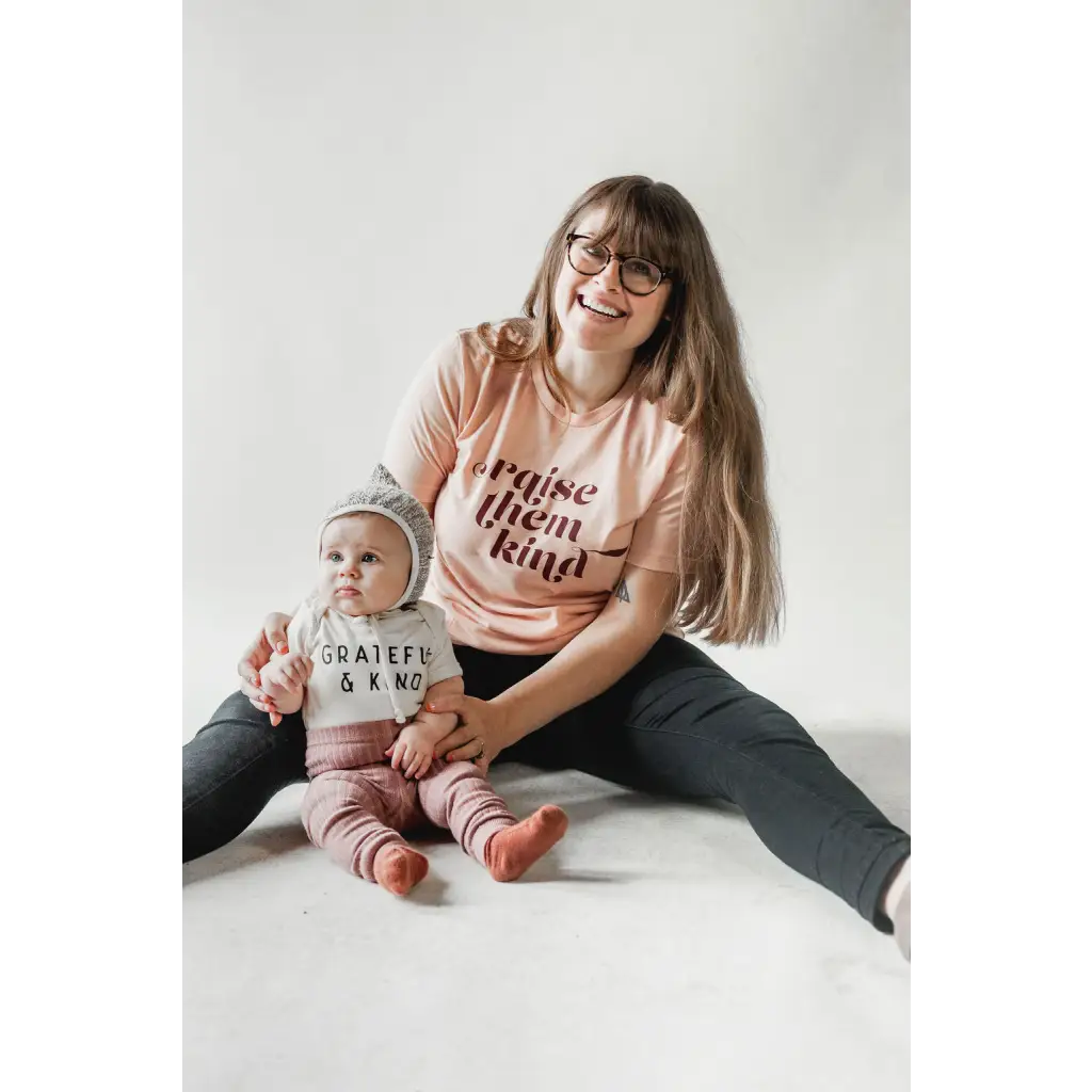 Parent and baby in matching Raise Them Kind organic cotton graphic t-shirts, cozy together