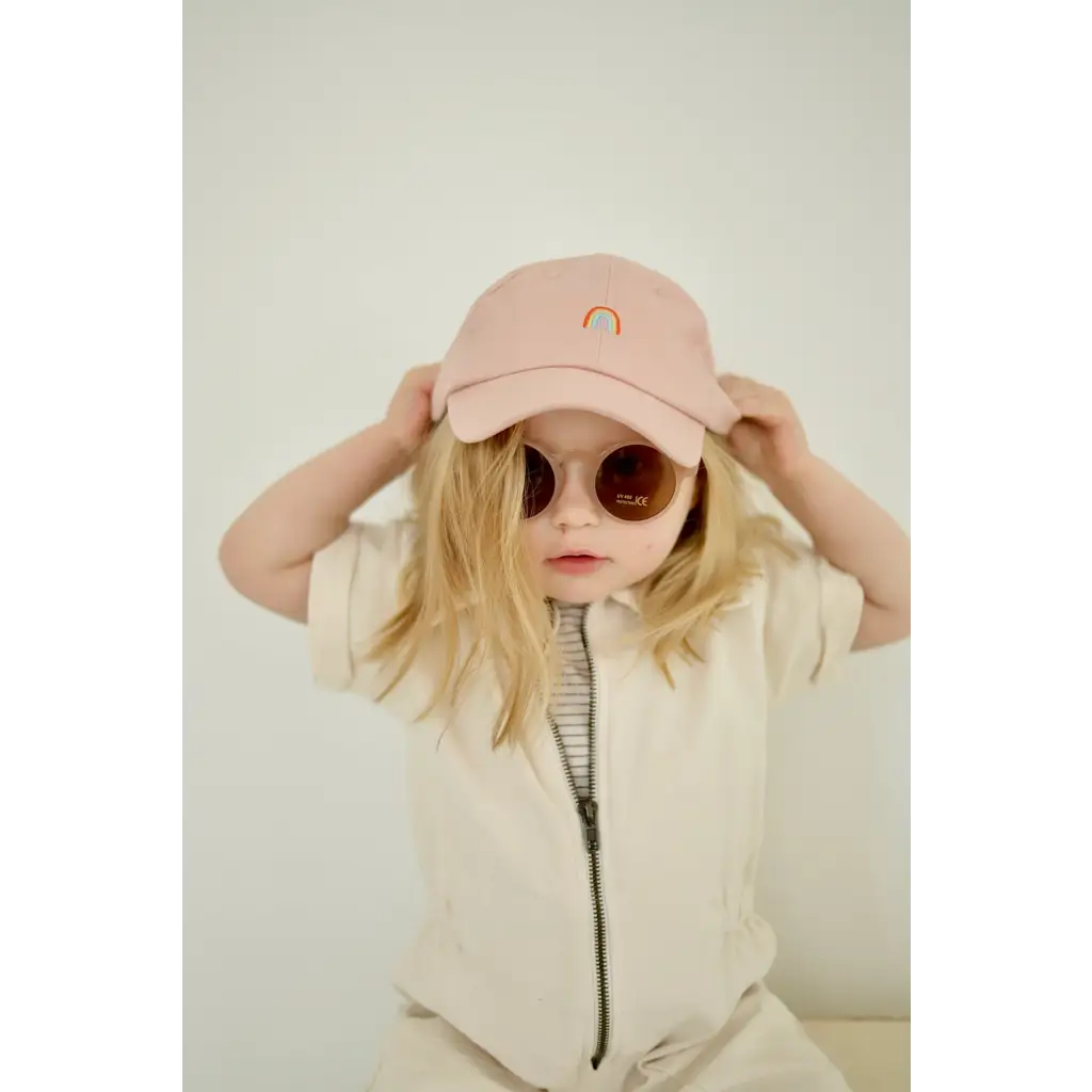 Pink baseball cap with rainbow emblem worn with adorable round sunglasses for kids