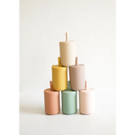 Six pastel cylindrical candles stacked in a pyramid near mini silicone straw cups