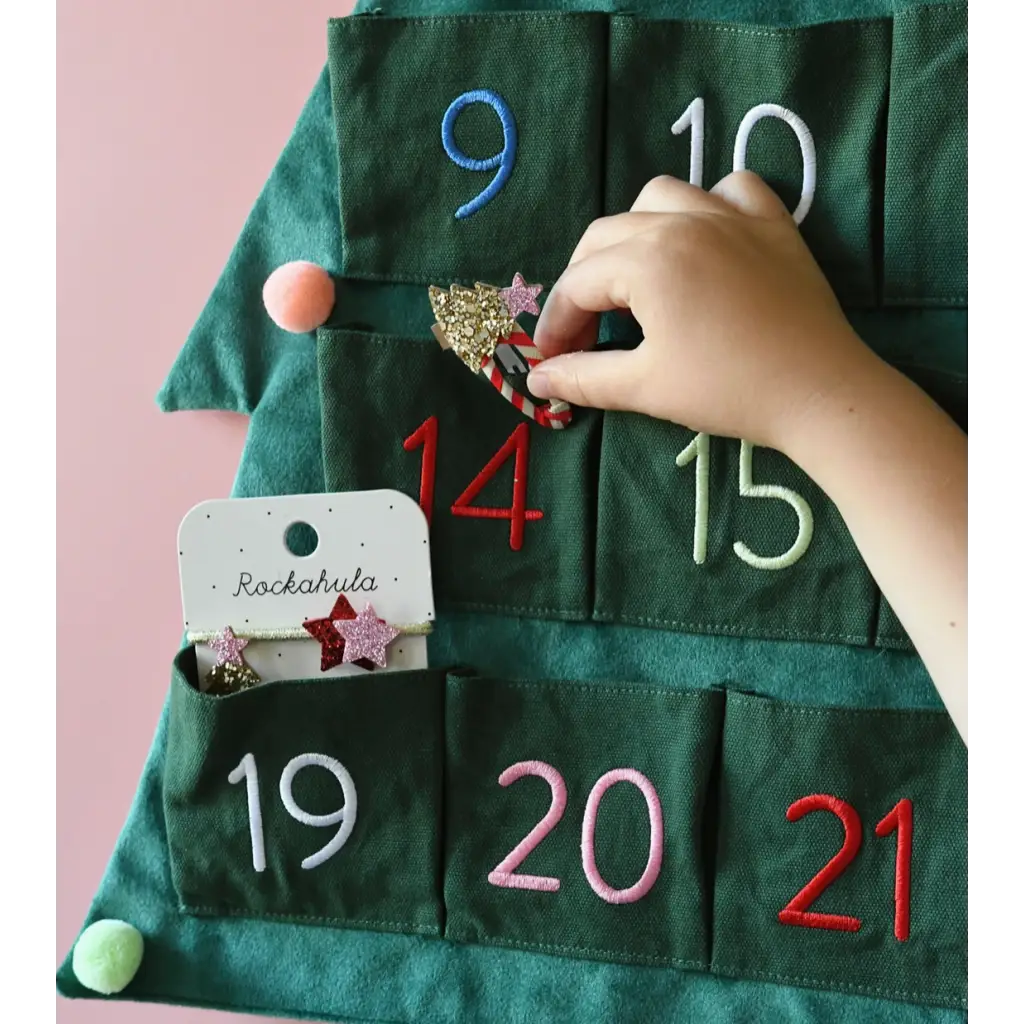 Hand placing a surprise in a green fabric advent calendar with Stripy Christmas Tree Ponies