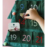 Hand placing a surprise in a green fabric advent calendar with Stripy Christmas Tree Ponies