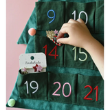 Hand placing a surprise in a green fabric advent calendar with Stripy Christmas Tree Ponies