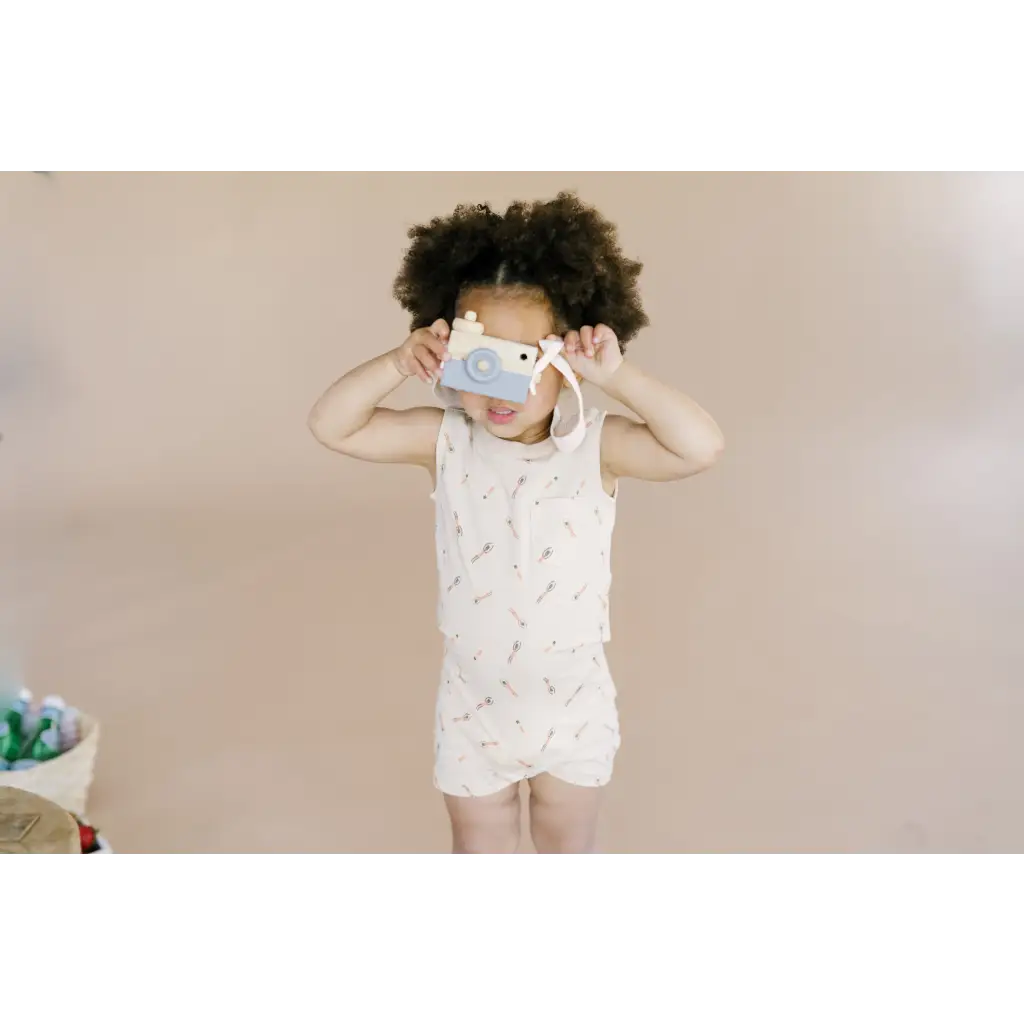 Child in a white patterned romper and face mask, rocking the pocket playsuit vibe