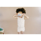Child in a white patterned romper and face mask, rocking the pocket playsuit vibe