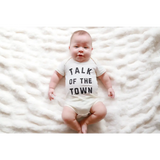 Baby in a white onesie saying TALK OF THE TOWN, made of soft organic cotton