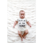 Baby in a white organic cotton onesie saying Talk of the Town for stylish newborns