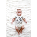 Baby in a white organic cotton onesie saying Talk of the Town for stylish newborns