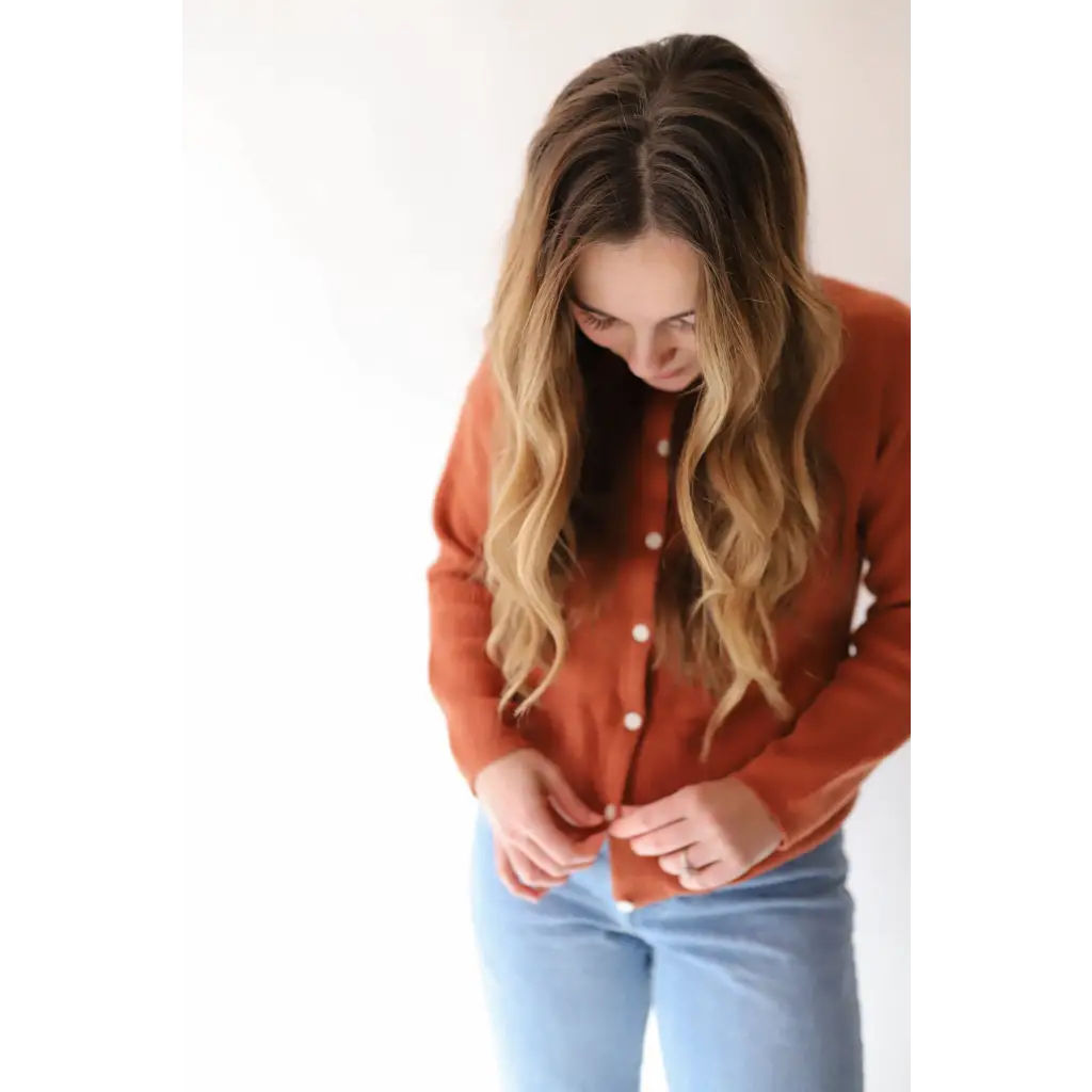 Rust-colored Annie Cardigan Sweater with white buttons over light blue jeans