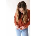 Rust-colored Annie Cardigan Sweater with white buttons over light blue jeans