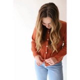 Rust-colored Annie Cardigan Sweater with white buttons over light blue jeans