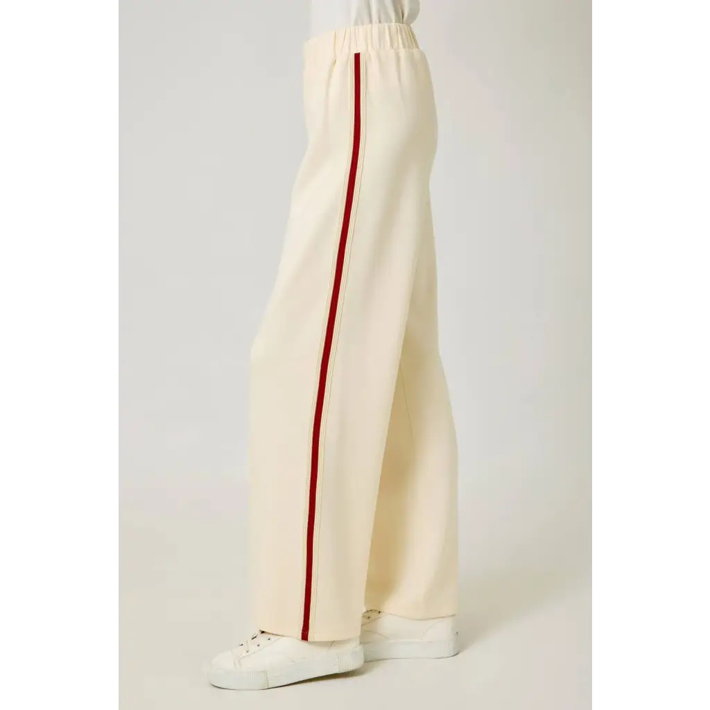 Cream-colored tracksuit pants with red stripes and elastic waistband, perfect for casual style