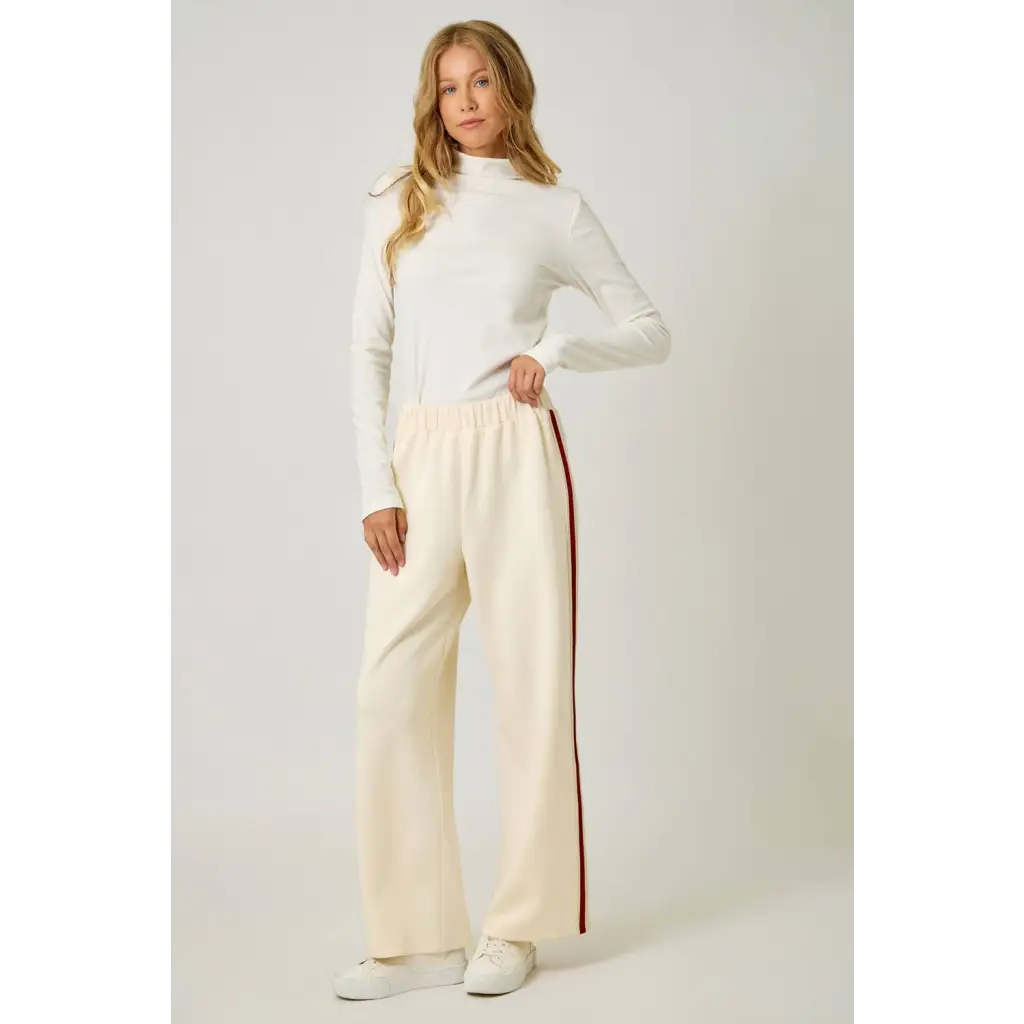 Cream-colored tracksuit pants with red side stripe and white sneakers for a casual look