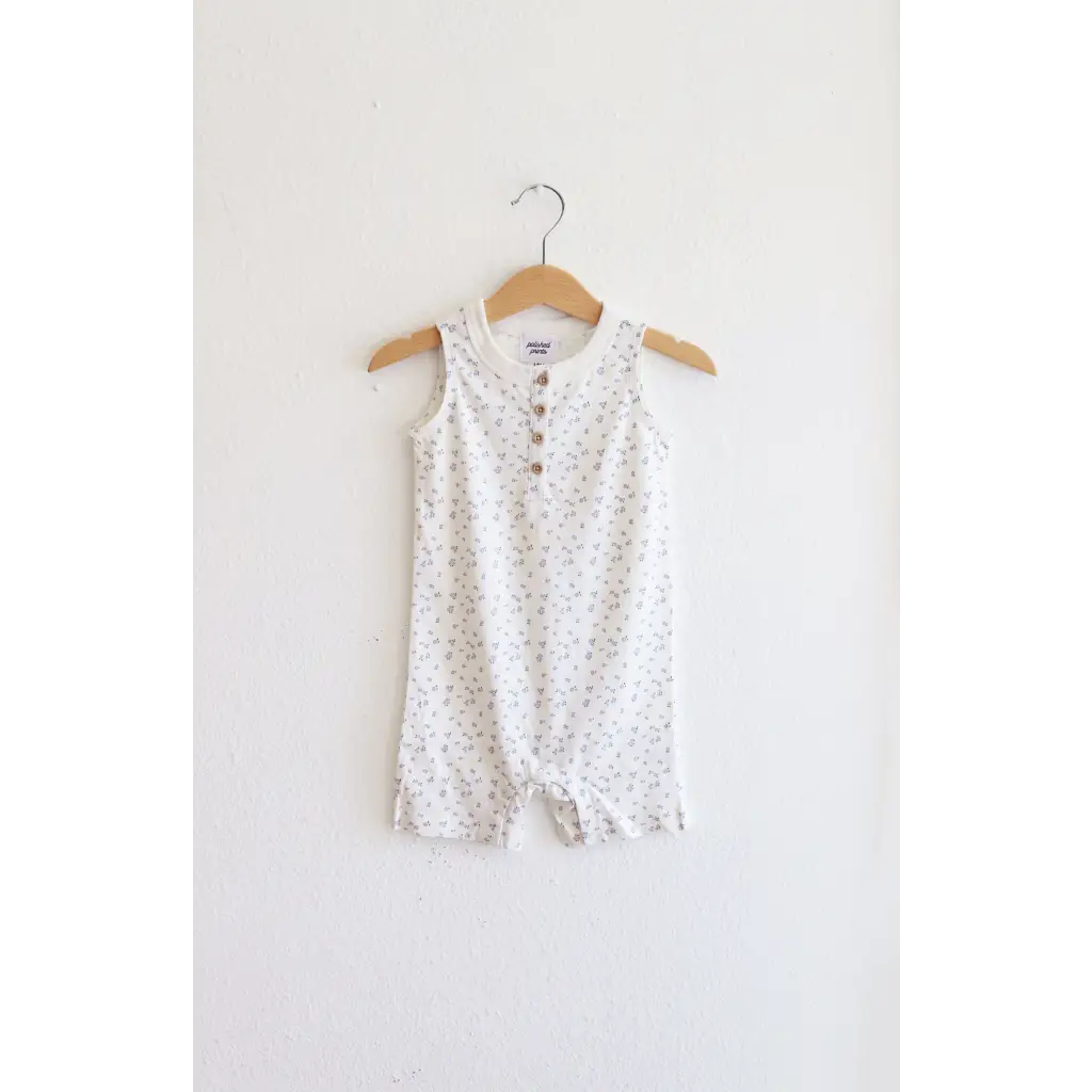 White sleeveless henley romper with polka dots hanging on a wooden hanger. Super soft organic cotton