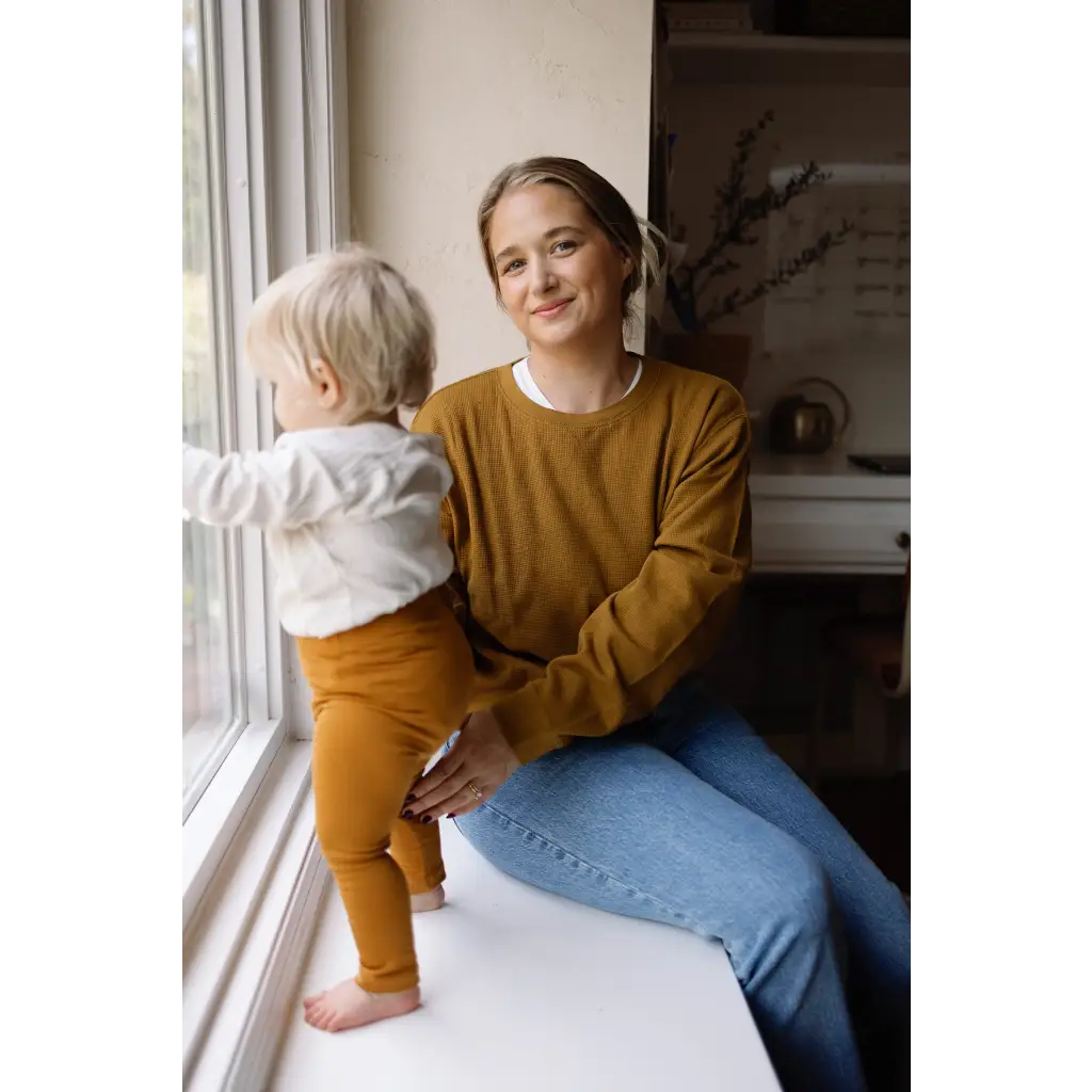 Person in a mustard yellow Jenna Knitted Waffle longsleeve pullover by a window with child