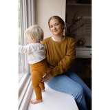 Person in a mustard yellow Jenna Knitted Waffle longsleeve pullover by a window with child