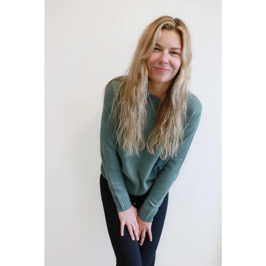 Person in a sage green Margo Crew Neck Sweater and dark pants, showing casual style