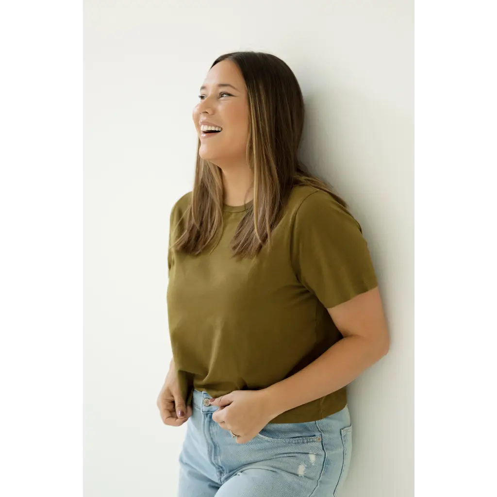 Person in an olive green mom crop boxy tee and light blue jeans laughing joyfully