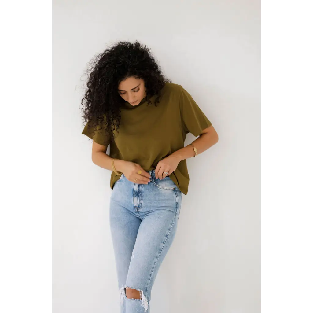 Curly-haired person rocks an olive mom crop boxy tee with ripped light blue jeans