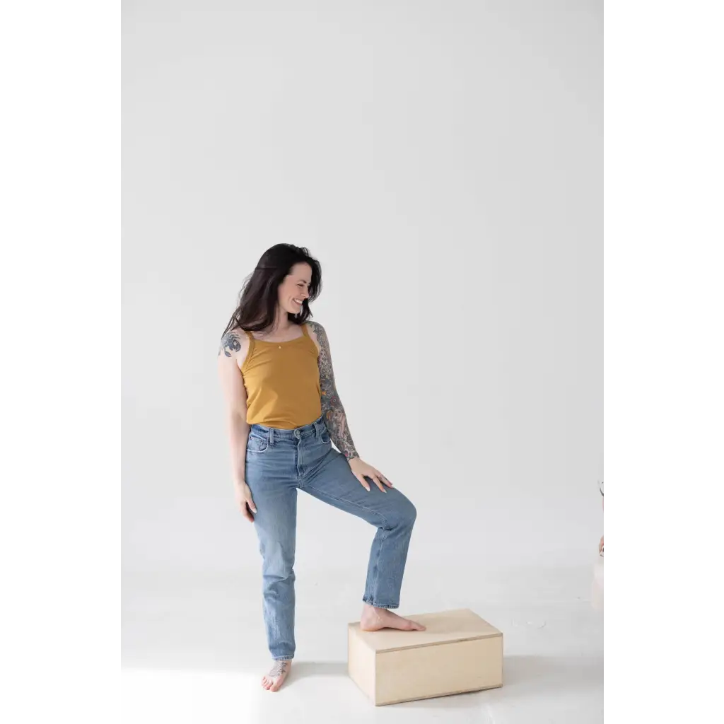 Person in a Mustard Yellow Mom Tank Top and blue jeans, a must-have for stylish womens clothes