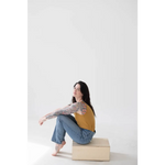 Person in a mustard yellow mom tank and blue jeans on a beige block, stylish womens clothes