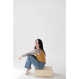 Person in a mustard yellow mom tank and blue jeans on a beige block, stylish womens clothes