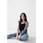Person in a jet black mom tank and blue jeans, showing off polished prints and tattoos