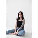 Person in a jet black mom tank and blue jeans, showing off polished prints and tattoos