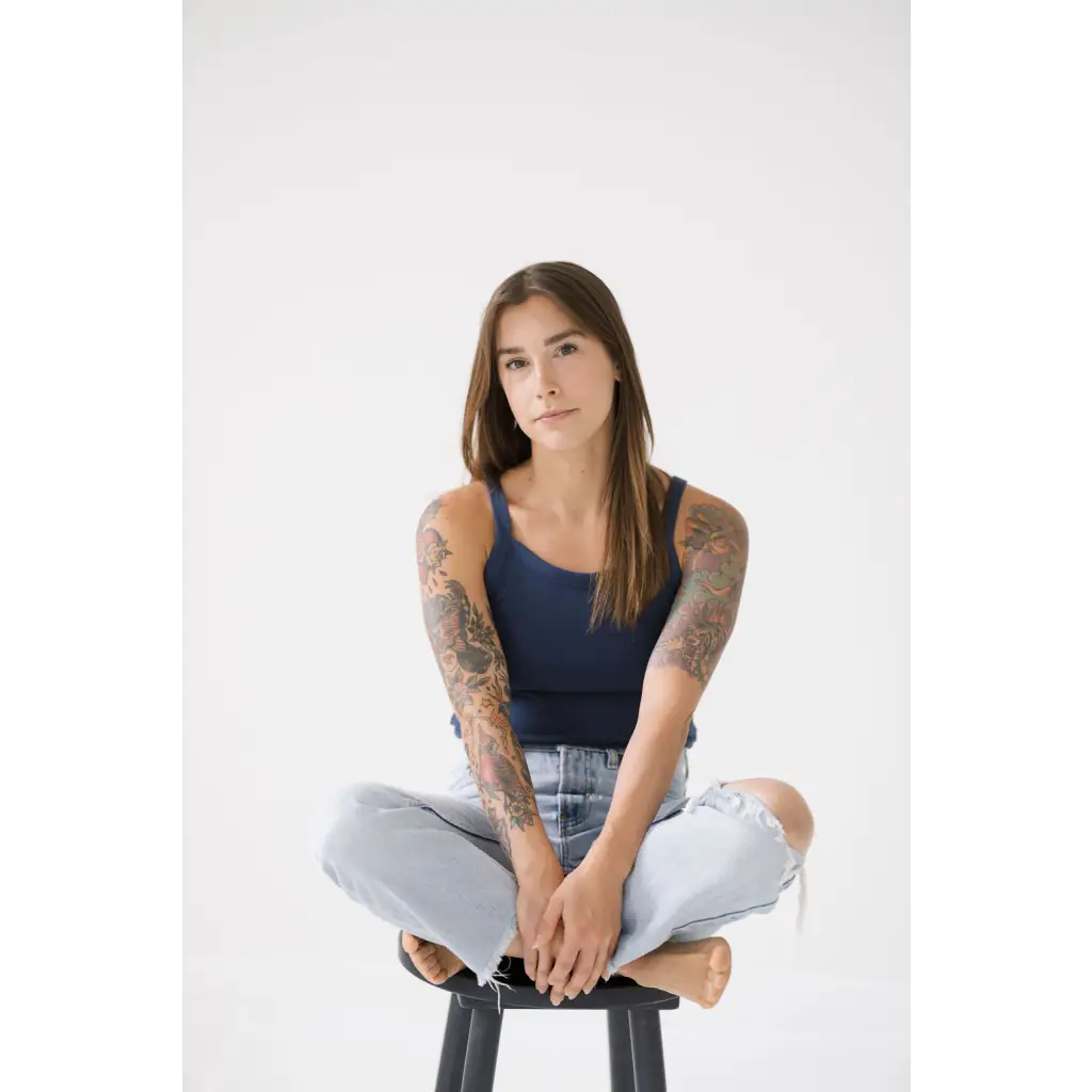 Person in a navy transitional mom tank and ripped jeans sitting on a stool