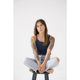 Person in a navy transitional mom tank and ripped jeans sitting on a stool