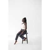 Person sitting on a black wooden stool wearing the Shifting Sand Mom Tank with Polished Prints
