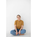 Person in a mustard yellow Mom Tee made of organic cotton and spandex blend, sitting cross-legged