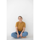Person in a mustard yellow Mom Tee made of organic cotton and spandex blend, sitting cross-legged