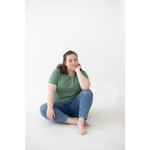Person in a green Mom Tee made of organic cotton and spandex blend sits cross-legged