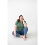 Person in a green Mom Tee made of organic cotton and spandex blend sits cross-legged