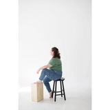 Person sitting on a black wooden bar stool wearing a comfy mom tee in organic cotton