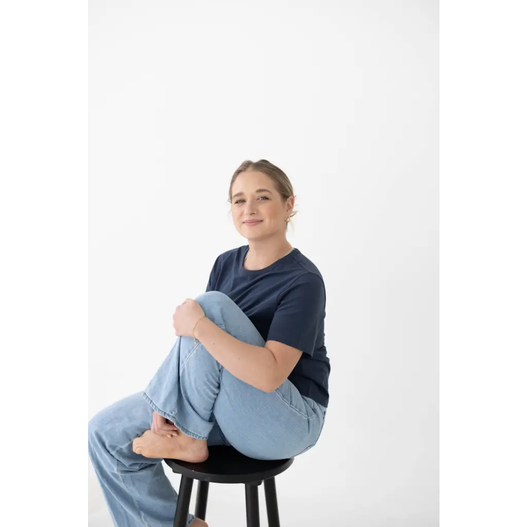 Person sitting on a black wooden stool, styled in a spandex blend mom tee and jeans