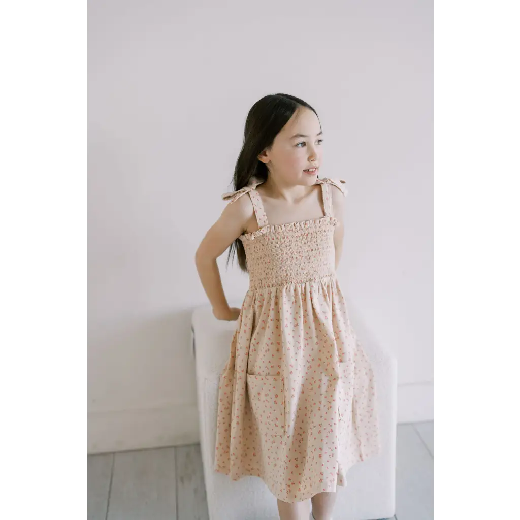 Cute peach-colored floral play dress with smocked bodice and shoulder ties for kids