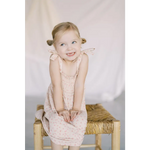 Child in a cute pale pink play dress sitting on a straw stool, perfect for summer fun