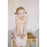 Child in a cute pale pink play dress sitting on a straw stool, perfect for summer fun