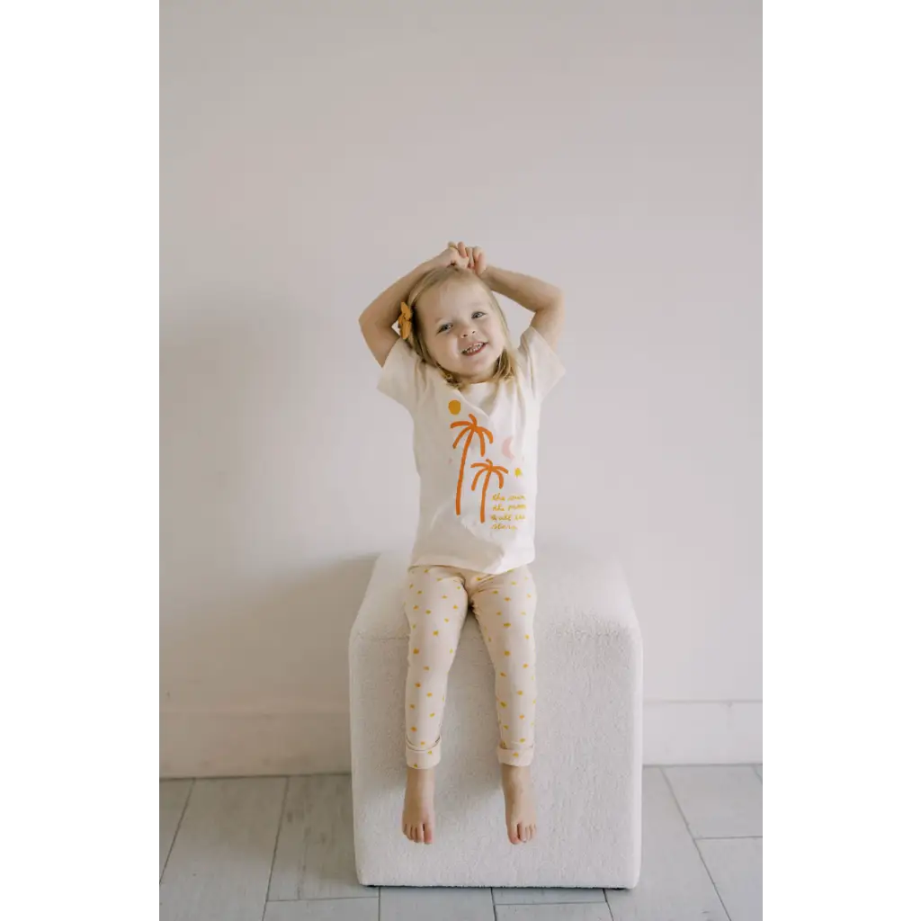 Child in cream pajamas with orange palm trees, perfect for dreams of distant galaxies