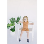Cute child in brown wearing a Henley Shorty Romper on a white wooden chair