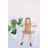 Cute child in brown wearing a Henley Shorty Romper on a white wooden chair